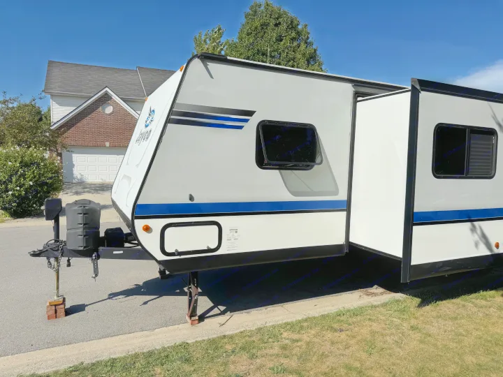 Brightly lit Jayco RV rental travel trailer with blue accents, parked on a residential street with its slide-out extended.. Jayco Jay Feather 2018