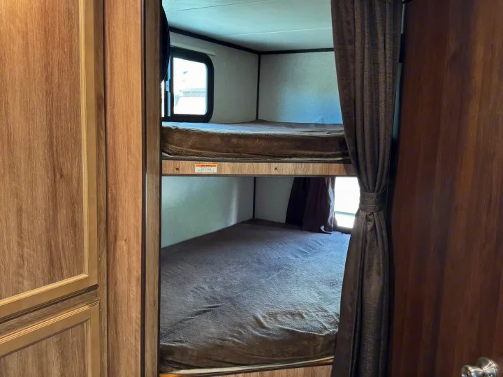 Explore this RV rental's sleeping area, featuring cozy bunk beds with blankets, a window, and privacy curtains for comfort.. Jayco Jay Feather 2018