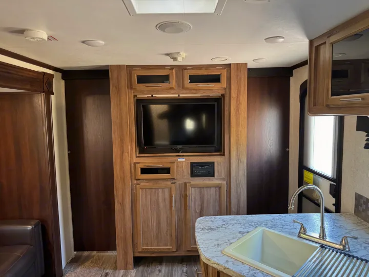 Inside this RV rental: a media console with TV & stereo, kitchen with sink & faucet, and rich wood cabinetry.. Jayco Jay Feather 2018