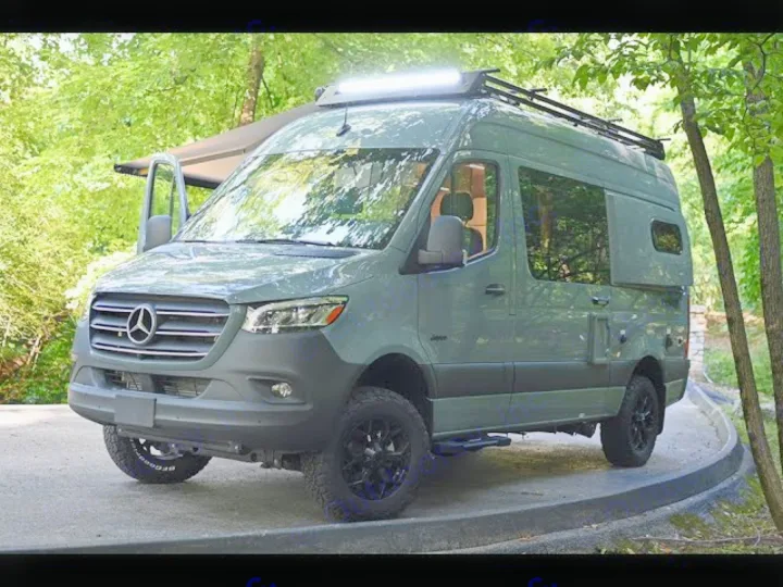 Rugged sage Mercedes-Benz Sprinter rv rental van with off-road tires, parked in a lush, green outdoor setting.. Jayco Terrain 2023