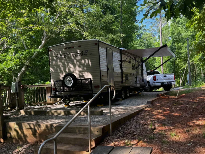 Grey Wolf RV rental set up at a wooded campsite with a truck and wooden deck, providing a shaded outdoor experience.. Forest River Cherokee Grey Wolf 2016