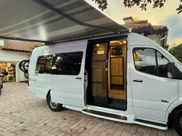 White camper van with extended awning, side door open to reveal a well-equipped interior, perfect for an rv rental trip.. Midwest Automotive Designs Midwest Automotive Designs Class B 2023