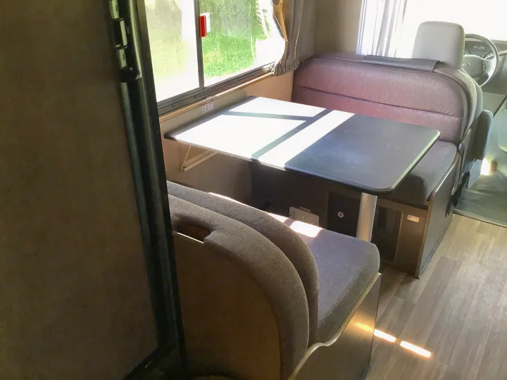 RV rental interior: a bright dinette with two cushioned benches, a table, and sunlight from the window. Great for dining/relaxing.. Thor Majestic 2018