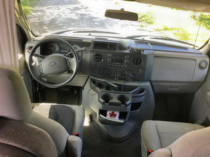 RV rental interior: Ford dashboard, steering wheel, console with cup holders, charging ports, and a MAX 90km/hr sticker.. Thor Majestic 2018