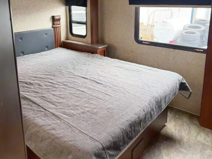 RV rental bedroom interior: large bed with gray spread, dark headboard, and windows showing outdoor tires. Ideal for rest.. Tioga Montara 2013