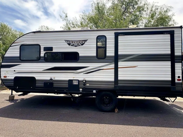 This Wildwood FSX rv rental is a light-colored travel trailer with grey stripes, parked on asphalt under a cloudy sky.. Forest River Wildwood FSX 2022