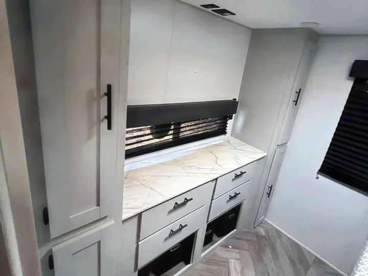 RV rental interior featuring light gray cabinets, a marble-look counter, dark window blinds, and tall storage units.. Forest River Wildwood FSX 2022