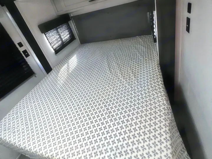 Comfortable RV rental bedroom with a gray patterned bed, window with blinds, and white/dark interior. Ideal for your journey.. Forest River Wildwood FSX 2022