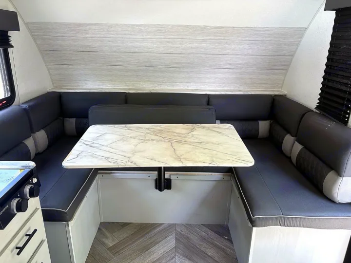 RV rental dinette: U-shaped dark gray benches, a white marble-patterned table, and light wood-look wall panels for cozy meals.. Forest River Wildwood FSX 2022