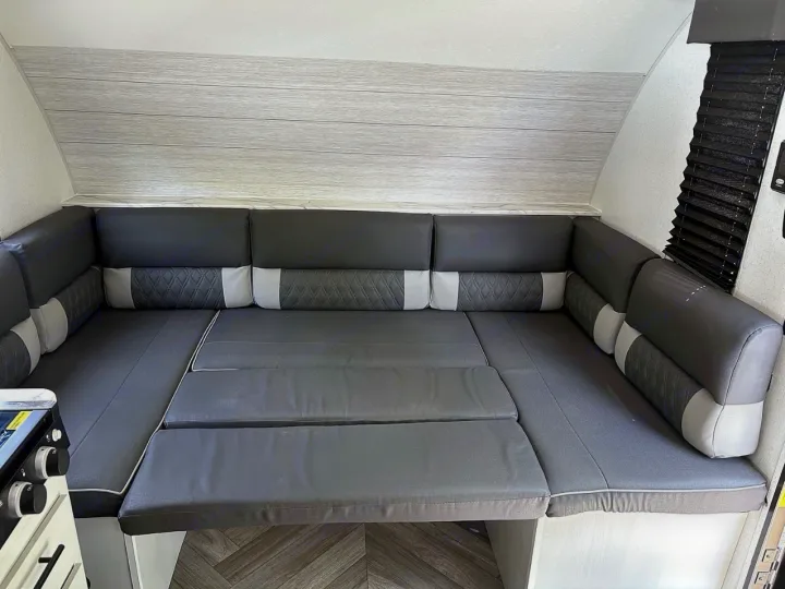 RV rental's cozy dinette with dark grey quilted cushions, convertible to a bed. Ideal camper seating for travel comfort.. Forest River Wildwood FSX 2022