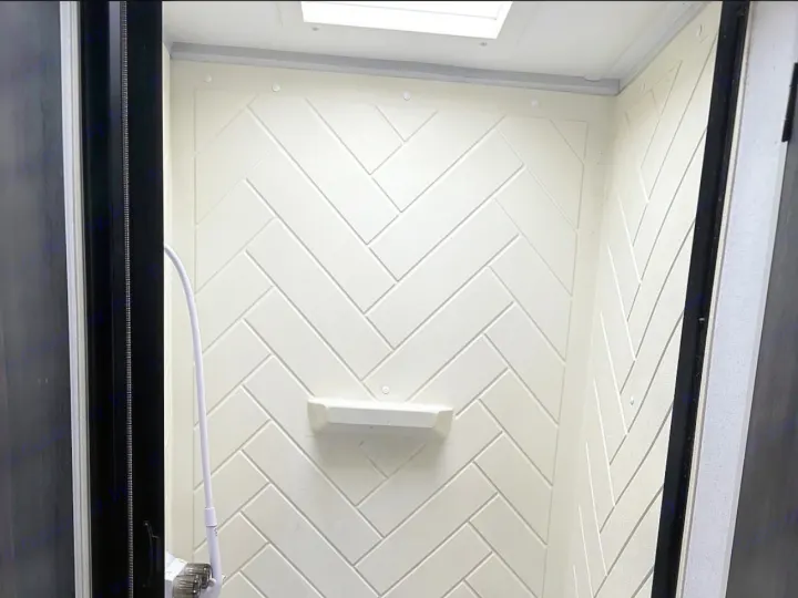 Inside a clean, compact RV rental shower featuring white herringbone wall panels, a built-in shelf, and a handheld shower.. Forest River Wildwood FSX 2022