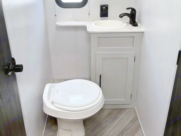 Compact RV rental bathroom featuring a white toilet, gray vanity with a sink and black faucet, and wood-look floor.. Forest River Wildwood FSX 2022