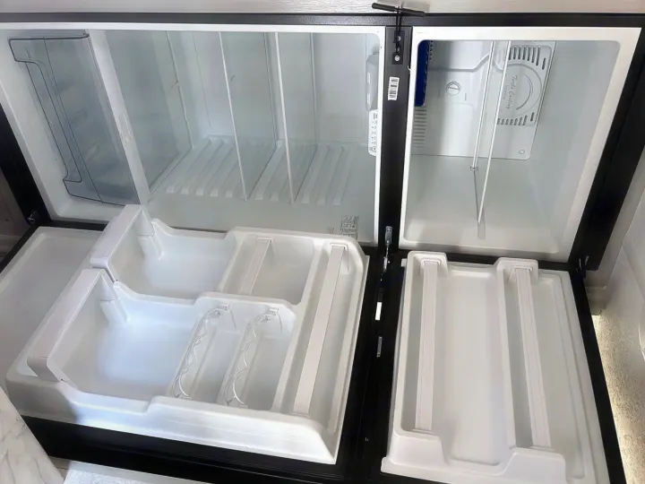Clean, empty RV rental refrigerator and freezer, doors open, shelves ready for your trip groceries.. Forest River Wildwood FSX 2022