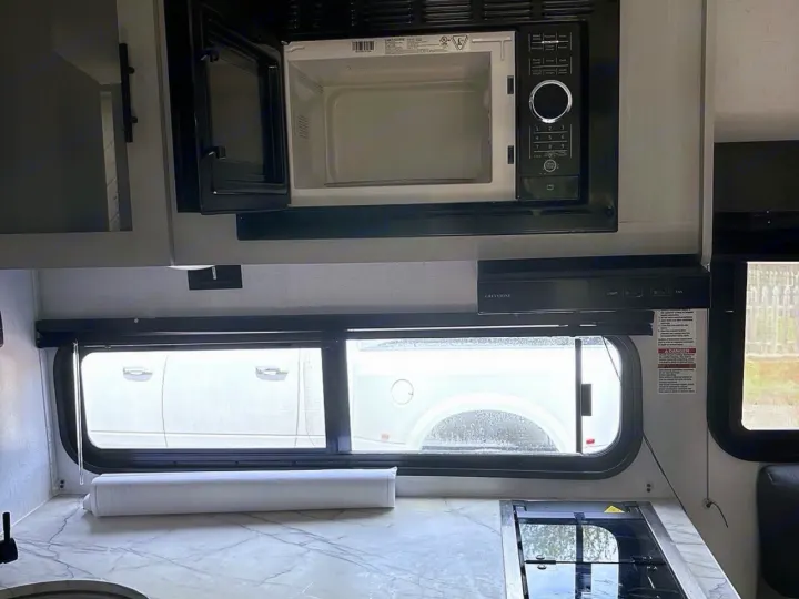 RV rental kitchen: open microwave, GreyStone vent hood, window, integrated cooktop, and marbled countertop.. Forest River Wildwood FSX 2022