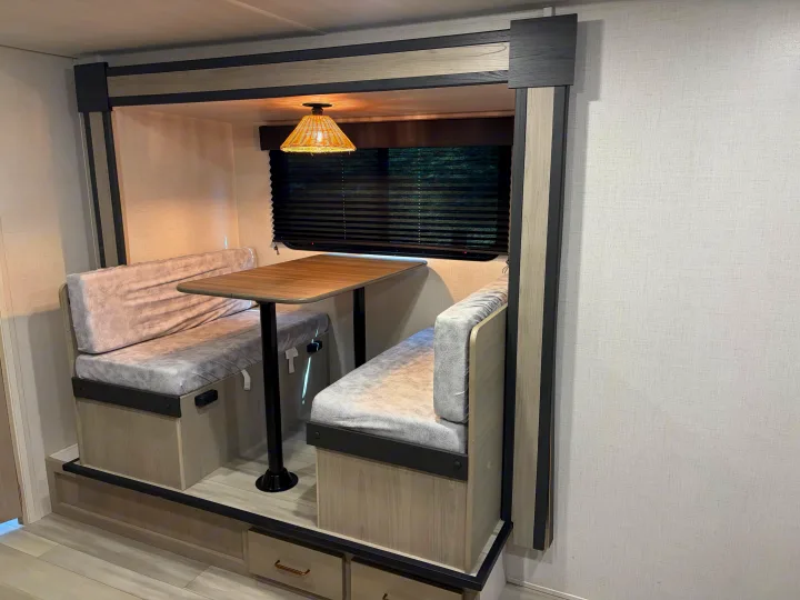 An RV rental dinette featuring comfortable gray benches, a wooden table, and a woven overhead light fixture.. Keystone RV Springdale 2024