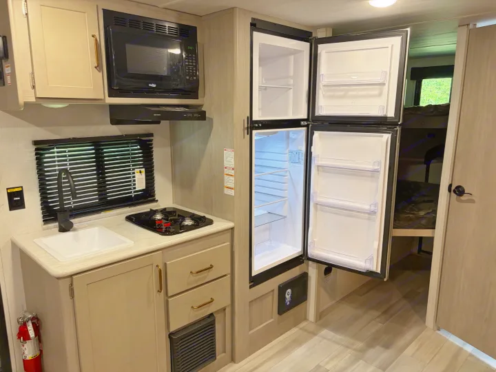 RV rental kitchen: a compact design with an open refrigerator, microwave, sink, stove, and bunk beds nearby.. Keystone RV Springdale 2024