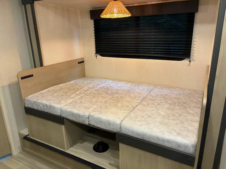 Inside an RV rental: a modern bed or dinette conversion with light wood trim, gray cushions, and a window blind.. Keystone RV Springdale 2024