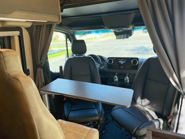 View inside an RV rental's front cabin, featuring a table between the swivel front seats and dashboard.. Jayco Terrain 2023