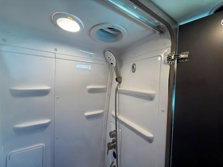 View inside an RV rental shower featuring a handheld shower head, ceiling light, vent, and built-in shelves.. Jayco Terrain 2023