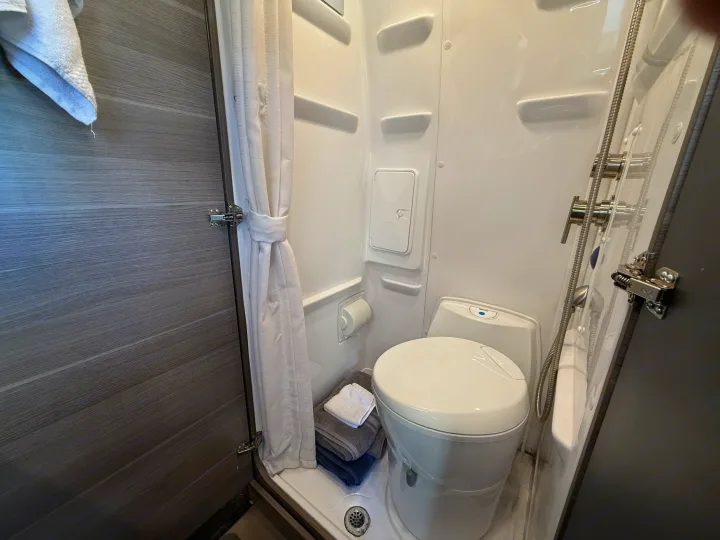 Compact RV rental bathroom featuring a toilet, shower with curtain, and folded towels.. Jayco Terrain 2023