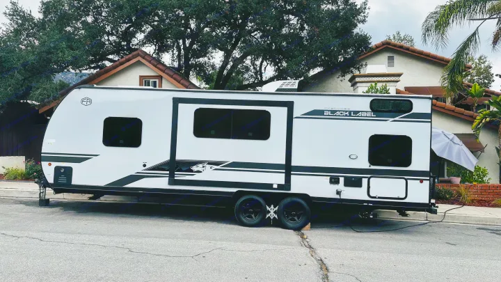 A white and black Cherokee Black Label travel trailer, a great rv rental option, is parked on a residential street.. Forest River Cherokee Grey Wolf 2027