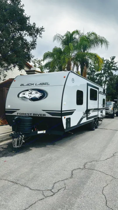 A Forest River Black Label Cherokee travel trailer, ideal for your next RV rental, parked on a street under an overcast sky.. Forest River Cherokee Grey Wolf 2027