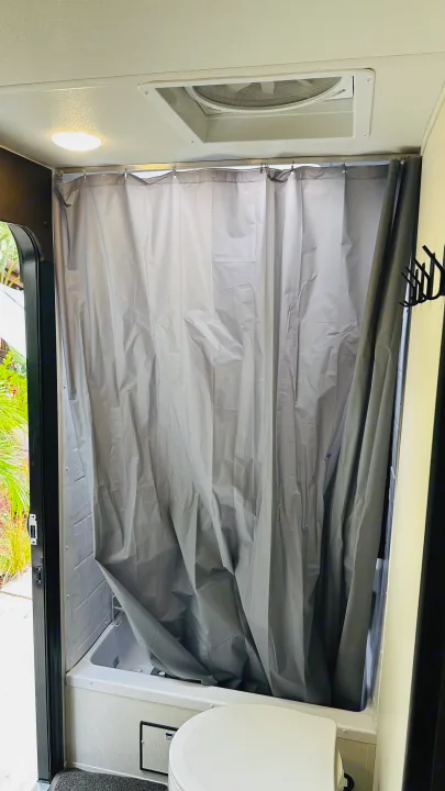 RV rental bathroom interior: compact shower with grey curtain, toilet, and ceiling vent fan visible.. Forest River Cherokee Grey Wolf 2027