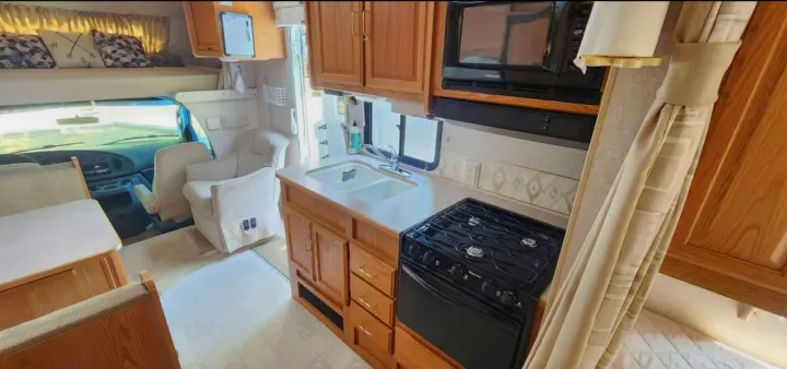 Inside this RV rental: kitchen with stove/sink, dining booth, driver's cab, and cozy overhead bunk. Ready for adventure!. Winnebago Minnie Winnie 2004