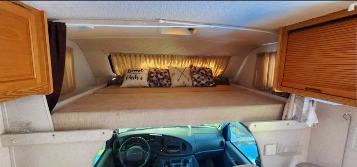 Inside an RV rental: a comfortable cab-over bunk with decorative pillows above the driver's cockpit area.. Winnebago Minnie Winnie 2004