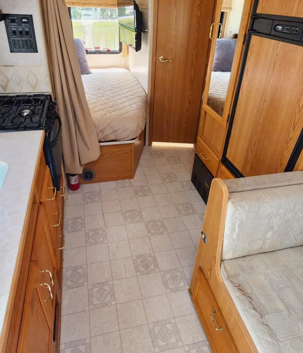 Bright rv rental interior featuring a compact kitchen with wood cabinets, a comfy bed, dinette, and patterned floor. Perfect for travel.. Winnebago Minnie Winnie 2004