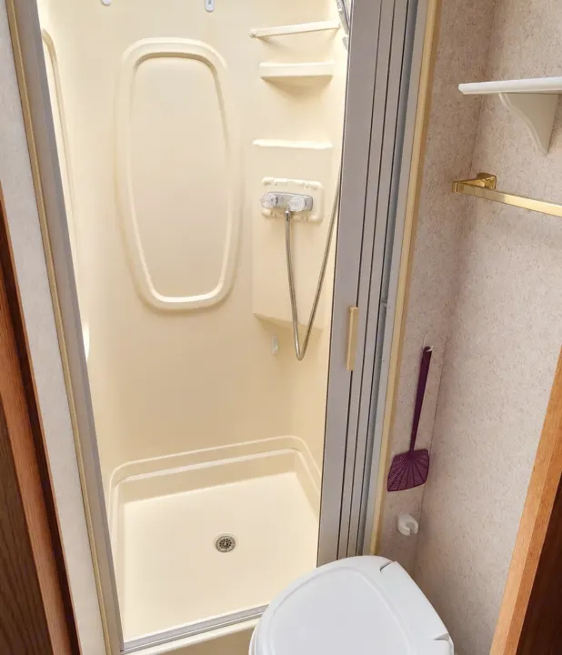 Compact RV rental bathroom: beige shower stall with handheld shower, small toilet, and folding door, optimized for travel.. Winnebago Minnie Winnie 2004