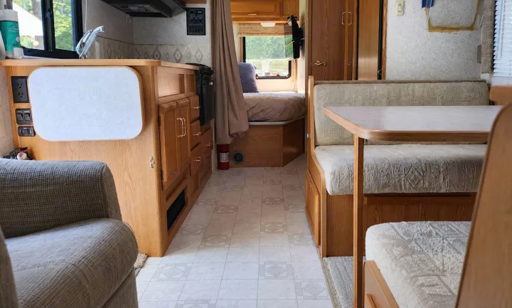 This RV rental interior features a kitchen counter, dinette with seating and table, and a rear bed, showing the living space.. Winnebago Minnie Winnie 2004