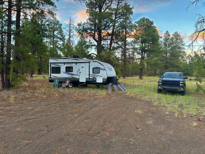 An RV rental travel trailer and pickup truck are parked in a forest clearing for boondocking, with solar panels.. Forest River Salem Cruise Lite 2018