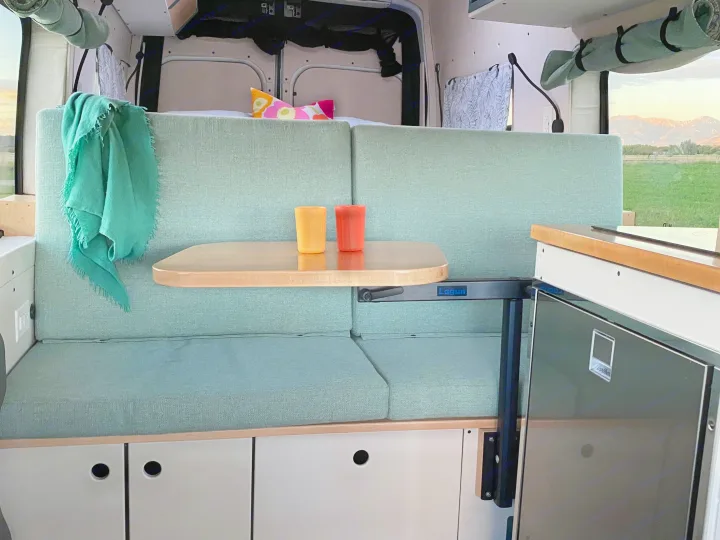 RV rental camper van interior featuring a green seating area, adjustable table, fridge, and scenic mountain views.. Ford Transit 2023