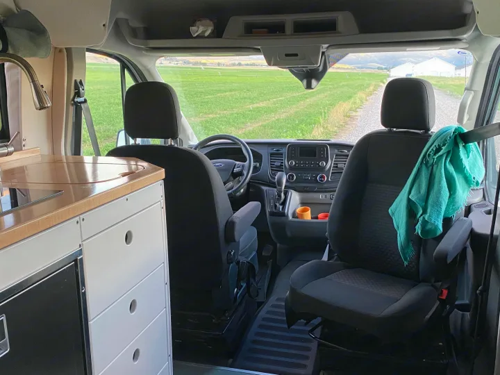 Experience van life in this RV rental! Modern camper van interior with kitchen, cockpit, & scenic green field views.. Ford Transit 2023