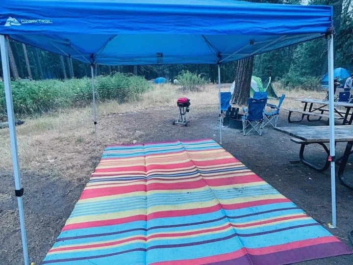 RV rental getaway: Blue canopy over a colorful mat, chairs, grill, & picnic table at a scenic wooded campsite.. Keystone RV Hideout 2009