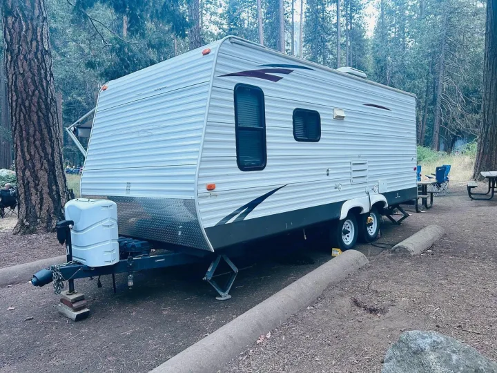 This RV rental, a white travel trailer, is set up at a tranquil forest campsite, ready for your outdoor adventure.. Keystone RV Hideout 2009