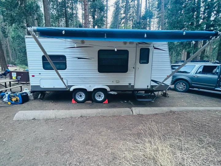 An RV rental parked at a forest campsite with its awning extended and lights, next to an SUV.. Keystone RV Hideout 2009