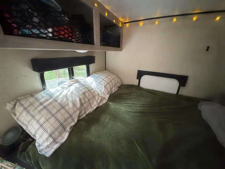 Cozy RV rental bedroom with plaid bedding, green blanket, storage nets, and string lights, perfect for camping.. Coachmen Apex Remote 16R 2023