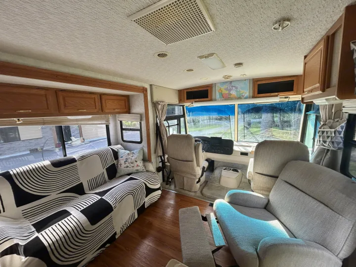 Cozy RV rental interior: black/white patterned couch, comfy chairs, driver's cabin, and scenic outdoor views.. Winnebago Brave 2004