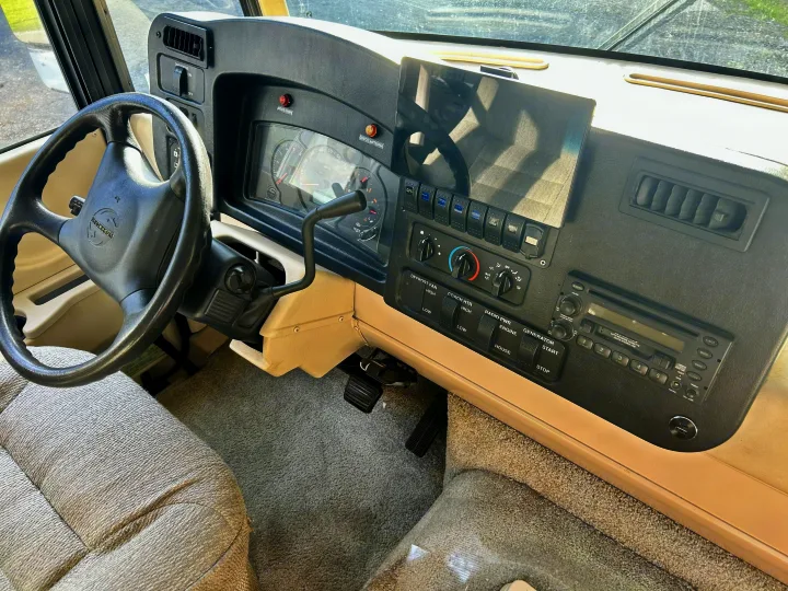 RV rental cockpit: dashboard with steering wheel, gauges, climate controls, and infotainment system, ready for adventure.. Winnebago Brave 2004