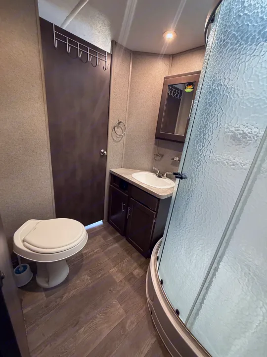 Compact rv rental bathroom with a curved glass shower, toilet, and sink vanity. Perfect for road trips.. Forest River Flagstaff Super Lite 2018