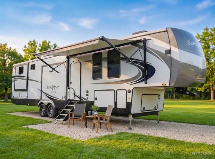 Spacious Sandpiper fifth-wheel RV rental set up on a gravel site with an awning & patio chairs, ready for adventure.. Forest River Sandpiper 2022