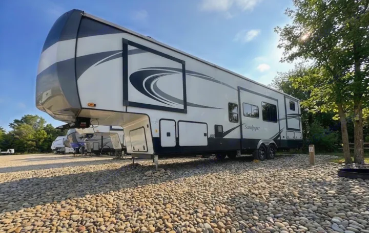 Modern Sandpiper fifth-wheel rv rental parked on a gravel campsite, ready for your next outdoor adventure.. Forest River Sandpiper 2022