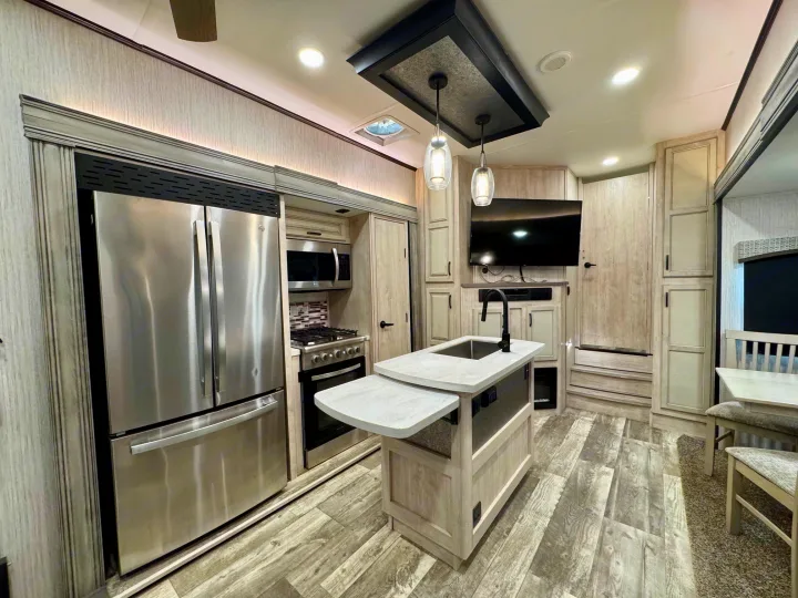 Spacious modern RV rental kitchen interior featuring stainless steel appliances, light wood-grain cabinets, and an island with sink.. Forest River Sandpiper 2022
