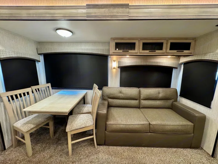 Comfortable RV rental interior with a light wood dining set, plush sofa, and storage cabinets, ready for your next adventure.. Forest River Sandpiper 2022
