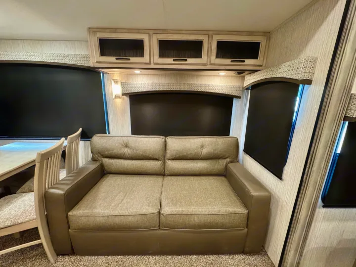 Comfortable RV rental living space with a two-seater sofa, overhead cabinets, and blackout window shades for privacy.. Forest River Sandpiper 2022