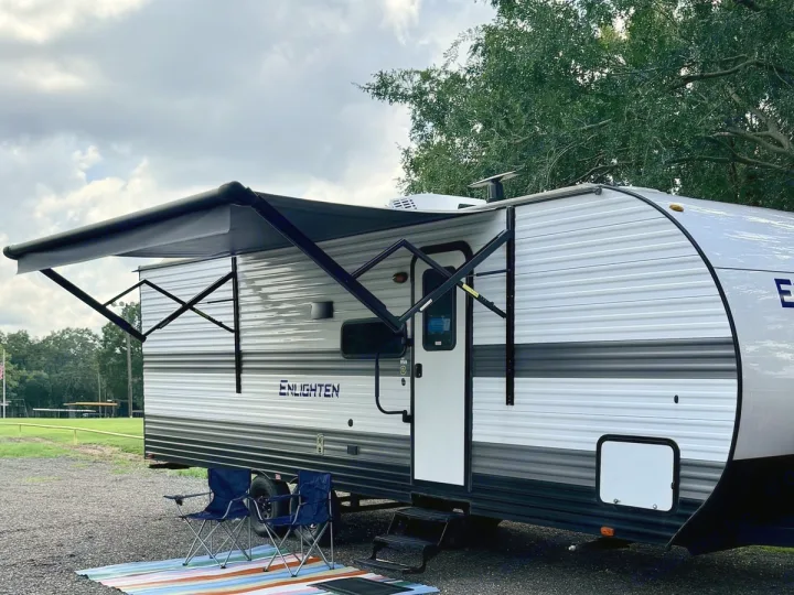 A white RV rental with an extended awning, blue chairs, and a colorful mat on gravel, perfect for relaxing travel.. Gulf Stream Enlighten SE 2025