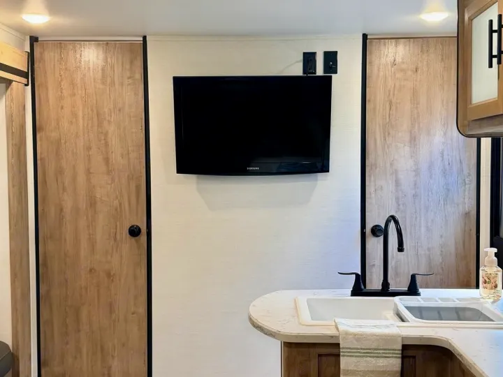 RV rental: Modern interior with a kitchen sink, black faucet, wall-mounted TV, and two light wood doors.. Gulf Stream Enlighten SE 2025