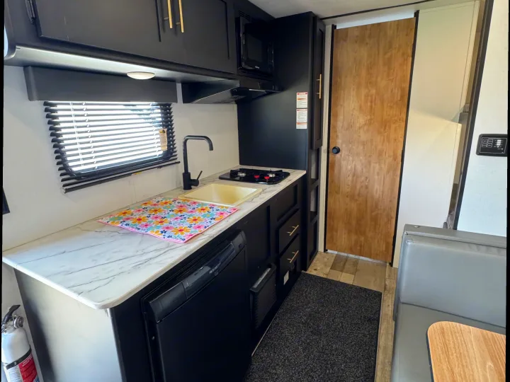 This RV rental's modern kitchen features sleek black cabinets, marble-look counters, a sink, stove, microwave, and dinette area.. Keystone RV Springdale 2022